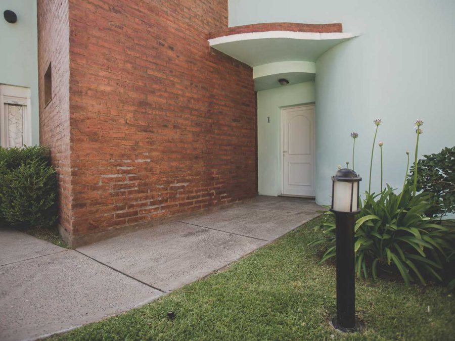 Ingreso a una cabaña con muro de ladrillo a la vista y cantero de agapantos